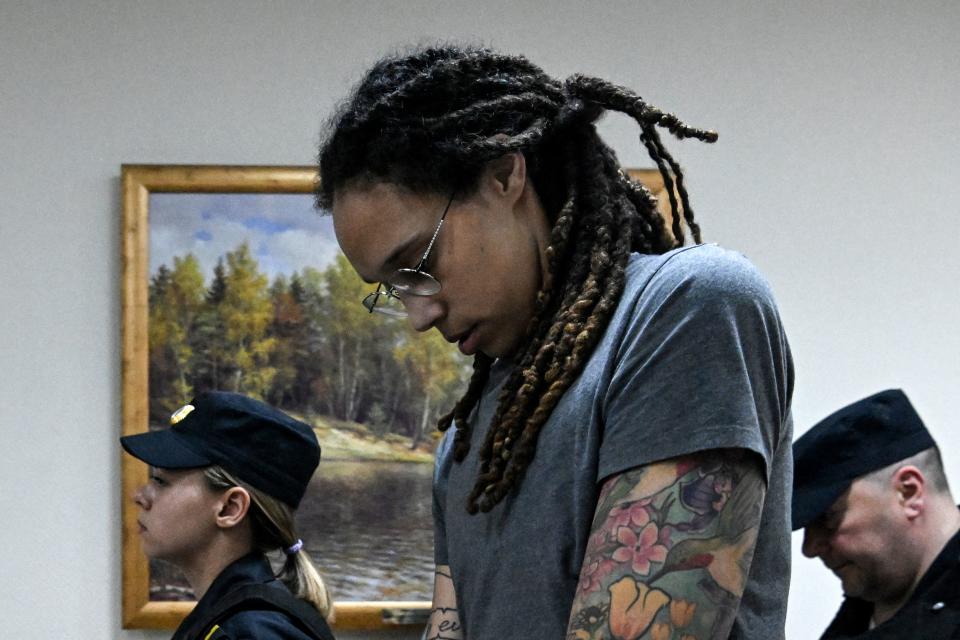 Brittney Griner, in profile, holds her head down near two people wearing uniforms.