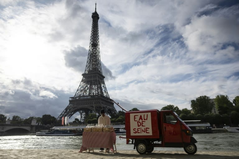 Un acolyte de l'artiste de rue James Colomina vend de l'eau en bouteille de la Seine devant la Tour Eiffel, à Paris le 10 juillet 2024 (Olympia DE MAISMONT)