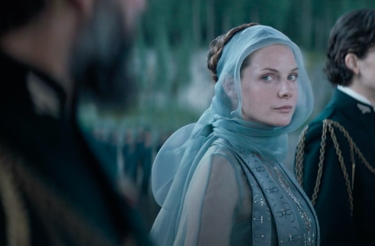 Still of Rebecca in "Dune," she wears a mesh blue headpiece and dress, cut off in the frame is Oscar Isaac to her left, who she is looking at, and Timothée