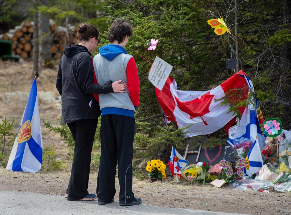 Visitors to a roadside memorial pay their respects in Portapique, Nova Scotia, on Friday, April 24, 2020. Royal Canadian Mounted Police say at least 22 people are dead after a man who at one point wore a police uniform and drove a mock-up cruiser, went on a murderous rampage in Portapique and several other Nova Scotia communities.