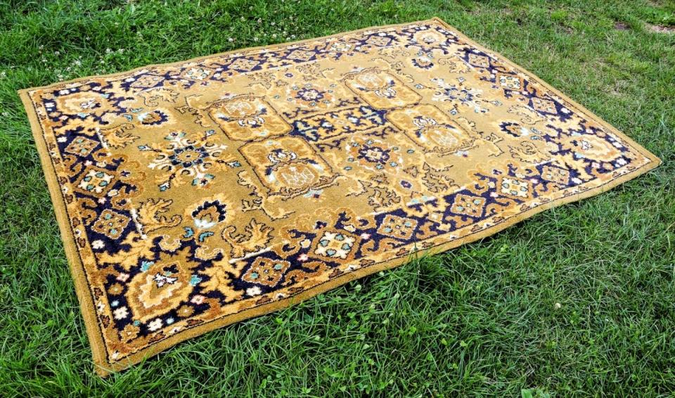 A gold and blue Persian rug laid out on a green grass lawn.