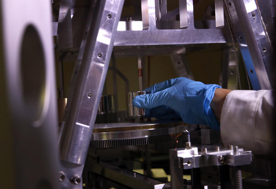 In this photo taken Wednesday, Oct. 17, 2018, Executive Secretary of the Consultative Committee for Mass and related quantities (CCM) Dr Hao Fang sets up a weight at the International Bureau of Weights and Measures, in Sevres, near Paris. The golf ball-sized metal cylinder at the heart of the world's system for measuring mass is heading into retirement. Gathering this week in Versailles, west of Paris, governments on Friday Nov. 16, 2018, are expected to approve a plan to instead use a scientific formula to define the exact weight of a kilo. (AP Photo/Christophe Ena)