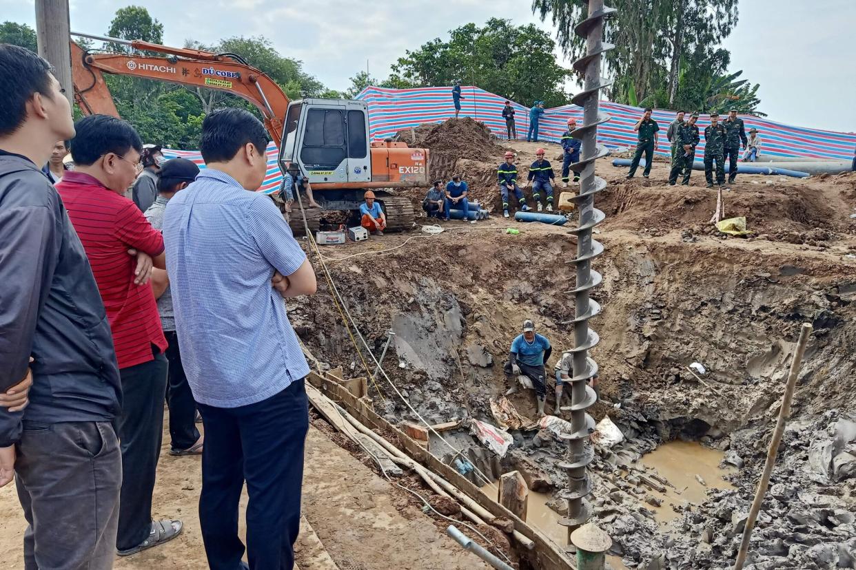 Rescuers look down into the site of where a 10-year-old boy is thought to be trapped in a 35-metre deep shaft at a bridge construction area in Vietnam's Dong Thap province on January 2, 2023. - Hundreds of rescuers in Vietnam battled January 2 to free a 10-year-old boy who fell into a 35-metre deep hole on a construction site two days ago.