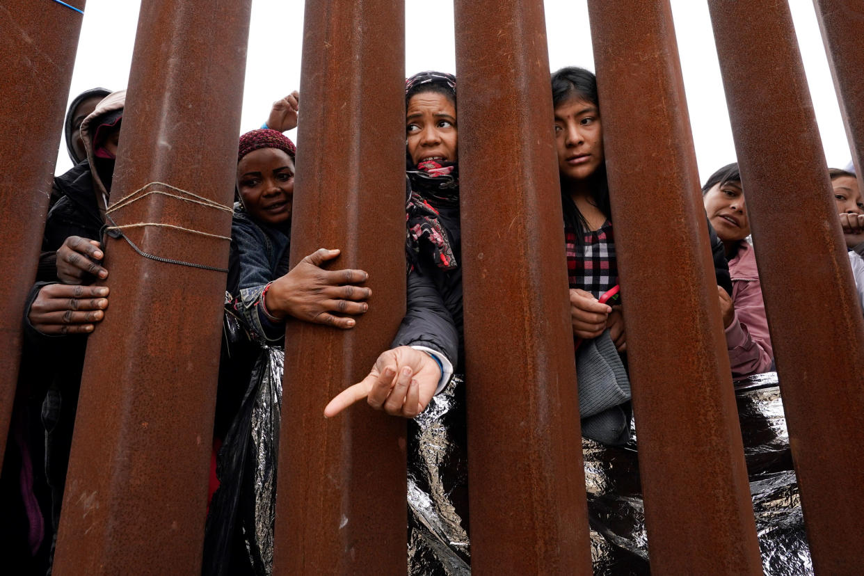 Migrants reach through a border wall for clothing handed out by volunteers, as they wait between two border walls to apply for asylum in San Diego