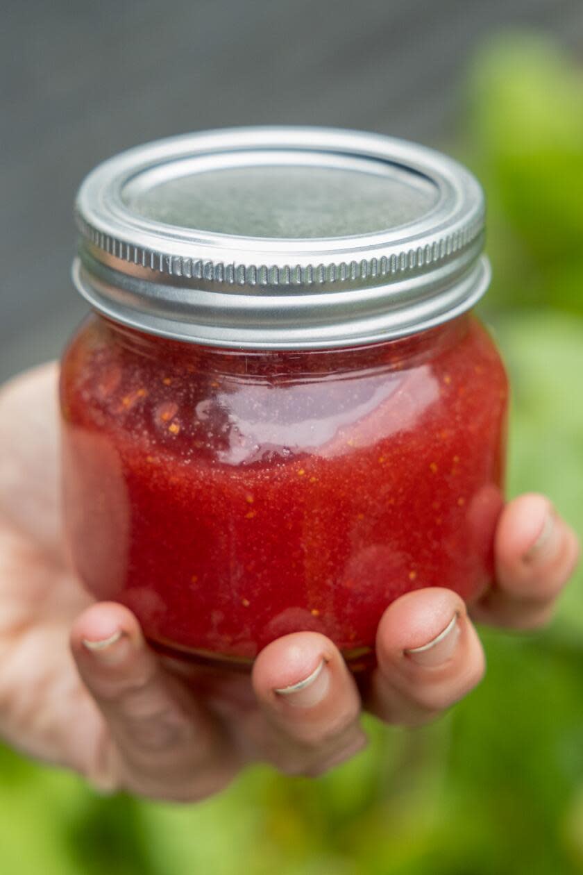 A hand holding a jar of red homemade jam.