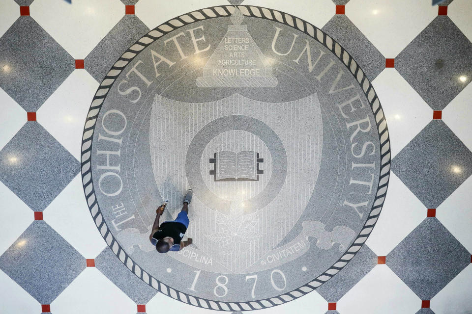 FILE - In this May 18, 2019 file photo a pedestrian passes through The Ohio State University's student union in Columbus, Ohio. Mike Drake, the president of The Ohio State University says he'll retire from that role next year. Drake's five-year tenure at one of the nation's largest universities has included strategic successes, such as record numbers for the school in applications, graduates, research expenditures and donor support. But it also has been marred by scandals involving the university's marching band, a prominent football coach and a former team doctor accused of widespread sexual abuse. (AP Photo/John Minchillo, File)