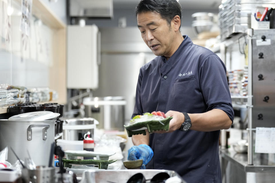 Katsumasa Okawa, owner of Okawa Fish Store, serves a fish dish to a customer at his restaurant in Iwaki, northeastern Japan on Friday, Aug. 25, 2023. Fish auction prices at a port south of the Fukushima Daiichi nuclear power plant Friday somehow dipped amid uncertainty about how consumers may respond a day after release to sea of treated and diluted radioactive wastewater began despite protests at home and in neighboring countries.(AP Photo/Eugene Hoshiko)