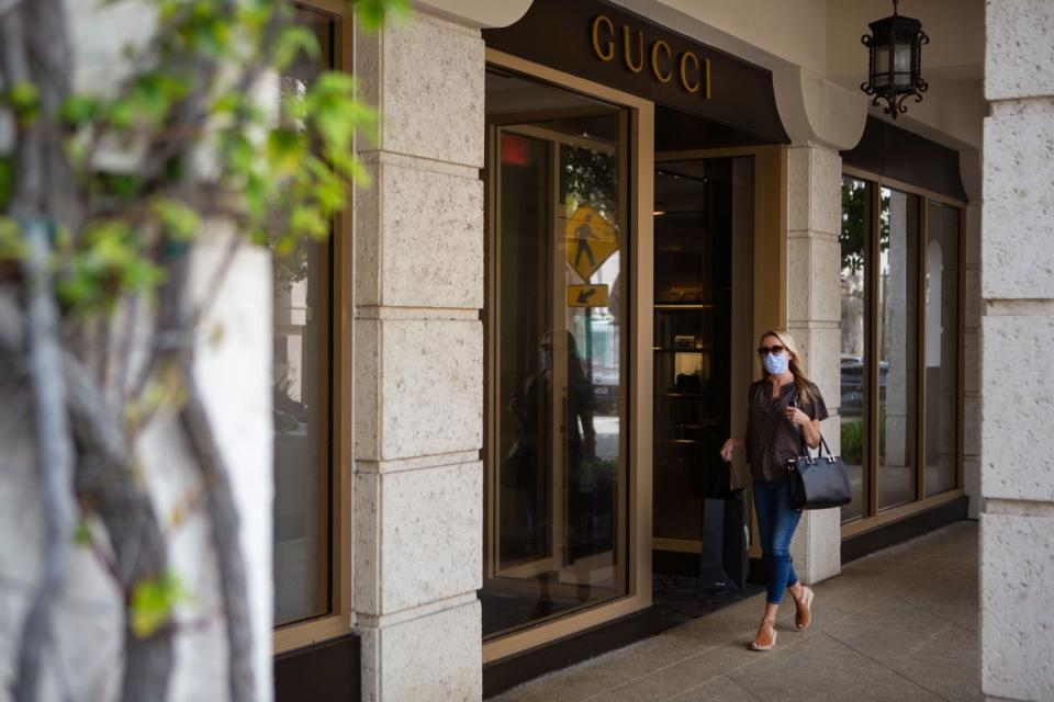 A pedestrian wearing a protective mask and carrying a purse walks past shops on Worth Avenue in Palm Beach.