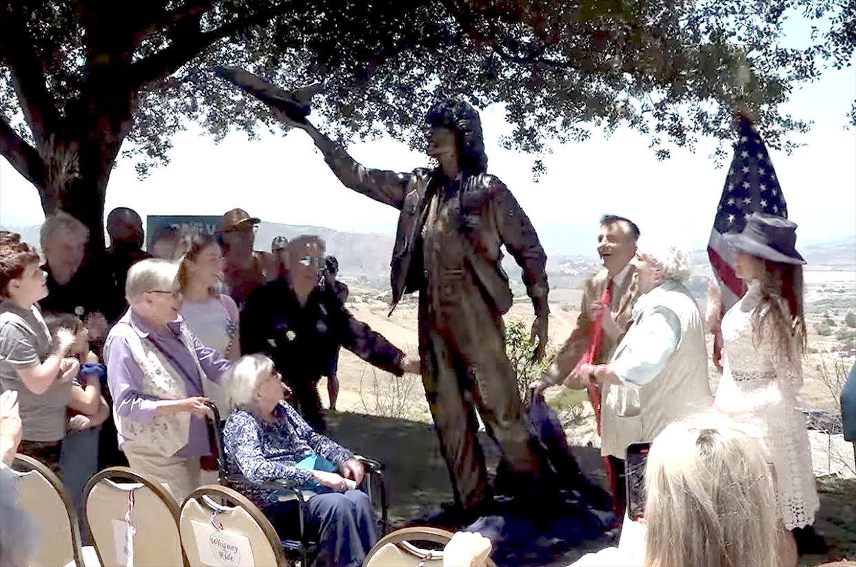  a crowd of people admire a bronze statue of sally ride with a tree and an american flag in the background 