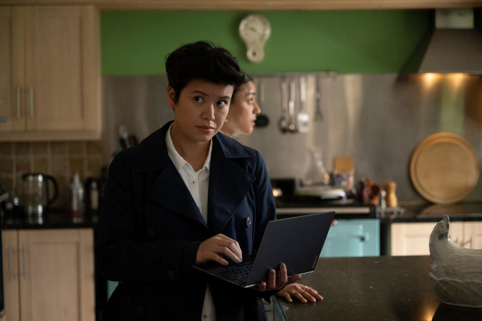 DC Blair Ferguson (Katie Leung) stands in a kitchen, typing on a laptop computer that she's holding with her other hand