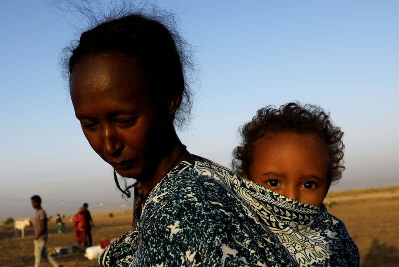 An Ethiopian woman who fled the ongoing fighting in Tigray region, carries her child near the Setit river on the Sudan-Ethiopia border in Hamdayet village in eastern Kassala state