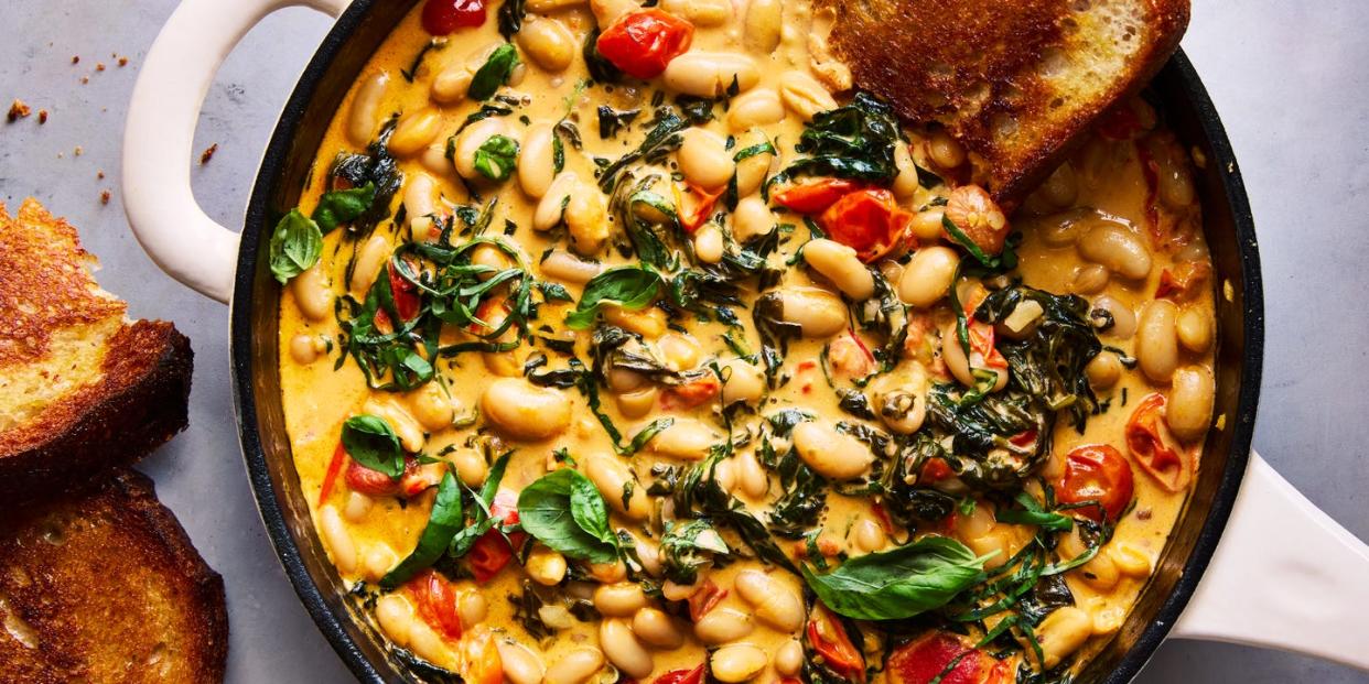 cast iron skillet filled with creamy tuscan white beans topped with basil, with toast alongside