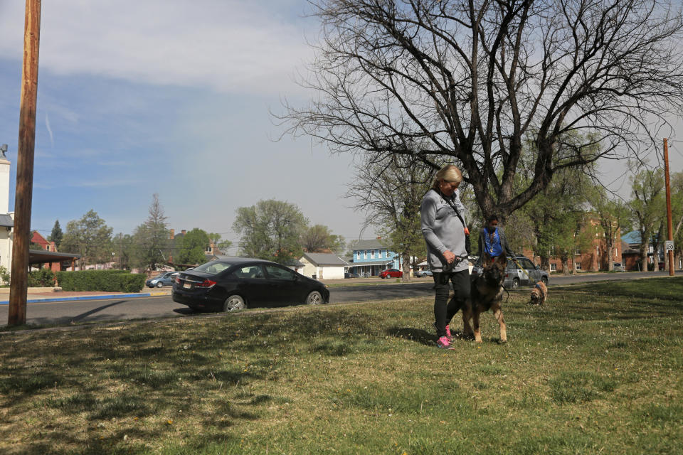 Liz Birmingham, 66, trains her dog Ciel at a class outside the Carnegie Library in Las Vegas, N.M., on Saturday, May 7, 2022. She said living in the city unnerving, as smoke and fire fluctuate with the winds, and some neighborhoods have been under evacuation advisories. The blue sky on the left is typical of New Mexico, while the haze on the right is from smoke from wildfires that have raged for over two weeks. (AP Photo/Cedar Attanasio)