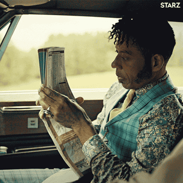 Orlando Jones as Mr. Nancy from the show "American Gods" is looking over a road map in a car