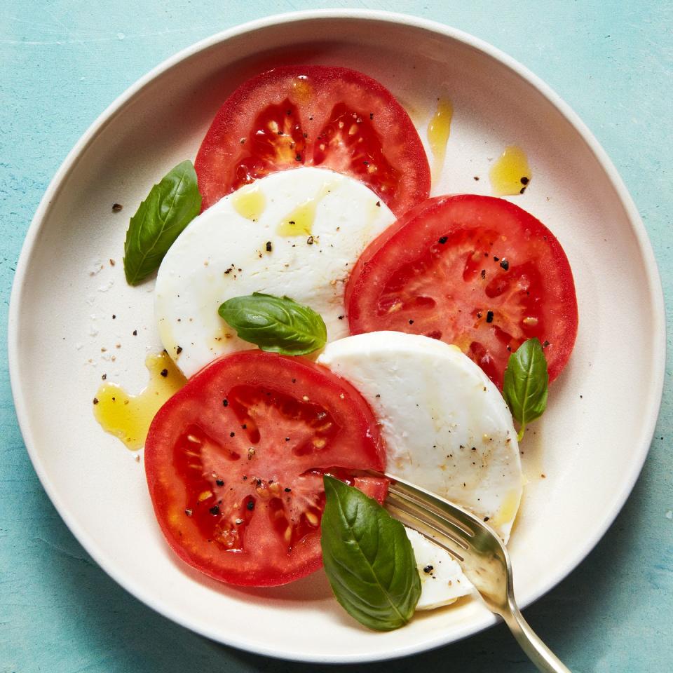 sliced tomatoes, mozzarella, and basil on a plate drizzled with olive oil