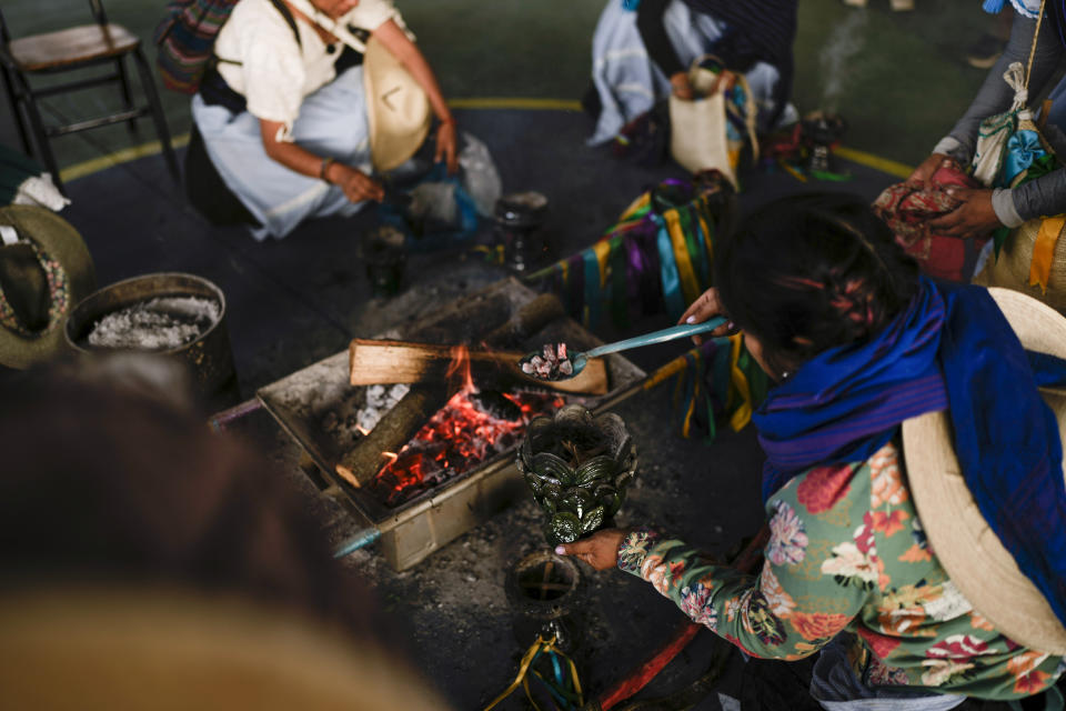 Mujeres indígenas purépechas alimentan sus incensarios de copal con carbón caliente durante una parada de descanso mientras caminan desde Erongarícuaro, donde los residentes mantuvieron viva una llama durante un año, hasta Ocumicho en el estado de Michoacán, México, el miércoles 31 de enero de 2024. (AP Foto/Eduardo Verdugo)