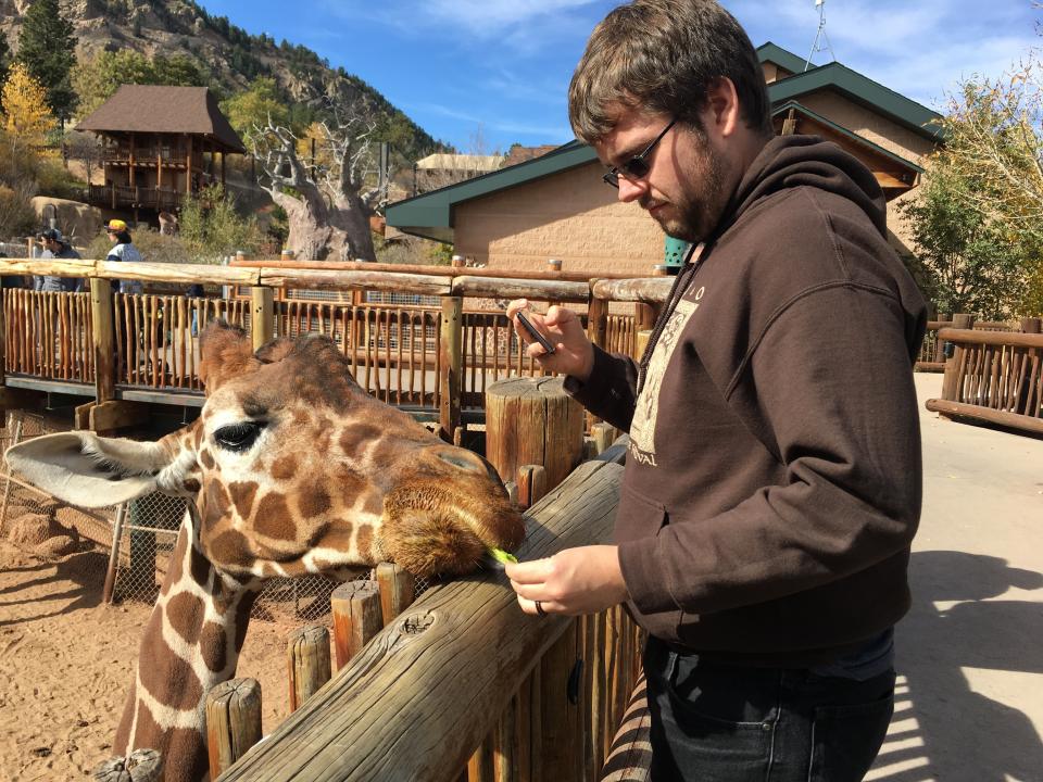 This Oct. 24, 2017 photo provided by Kayleigh Caskey shows her husband, Daniel Caskey feeding a giraffe at the Cheyenne Mountain Zoo while on a vacation in Colorado Springs, Co., that was funded by a wedding gift from one of the guests who attended their wedding. Millennials are changing the traditional wedding registry and are forgoing the traditional china and crystal and asking guests to contribute instead to honeymoon adventures, charitable causes and more. (Kayleigh Caskey via AP)