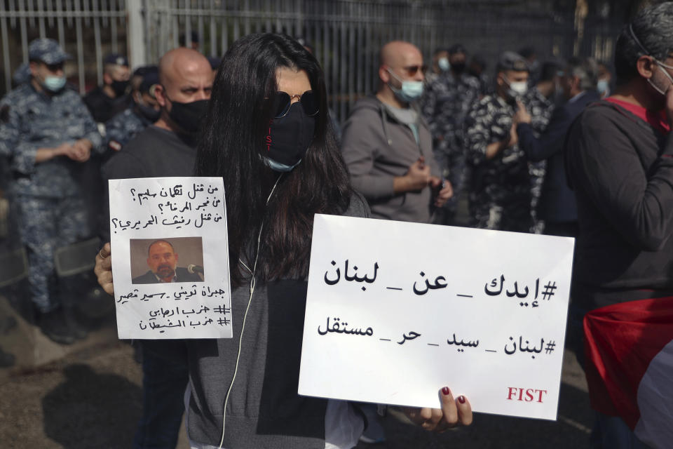 An anti-Hezbollah protester holds a picture of Lokman Slim, a longtime Shiite political activist and researcher, who has been found dead in his car, during a protest in front of the Justice Palace in BeirutBeirut, Lebanon, Thursday, Feb. 4, 2021. The Arabic words on posters read "Hands off Lebanon. Lebanon is sovereign, free and independent," right, and "Who killed Lokman Slim? Who bombed the port? Who killed Rafik Hariri, Gebran Tueni, Samir Kassir?" (AP Photo/Bilal Hussein)