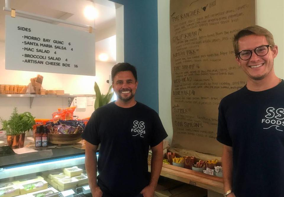 Alex Labastida, at left, and husband Alex Saleen pose for a picture by the wall-mounted menu for Seaside Foods deli inside the recently reopened Sebastian’s General Store in Old San Simeon Village on Friday, June 16, 2023. Kathe Tanner/ktanner@thetribunenews.com