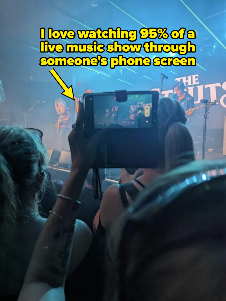 Person recording a concert on their phone with the band performing in the background