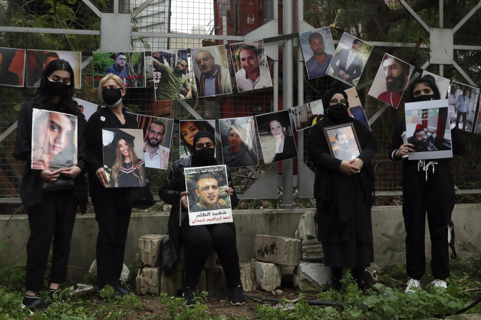 Relatives of the victims of the Aug. 4, 2020 Beirut port explosion hold portraits of their loved ones who were killed, Thursday, Feb. 4, 2021 in Beirut, Lebanon. The vigil at the seaport main entrance, marked six months since the blast that killed more than 200 people and injured thousands. The Arabic words on poster read "Who brought nitrates and for who? We have a right to know." (AP Photo/Bilal Hussein)