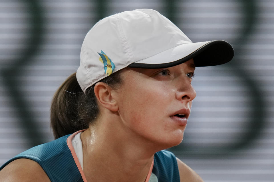 Poland's Iga Swiatek wears a ribbon with the colors of the Ukraine flag as she waits for the service of Ukraine's Lesia Tsurenko during their first round match at the French Open tennis tournament in Roland Garros stadium in Paris, France, Monday, May 23, 2022. (AP Photo/Thibault Camus)