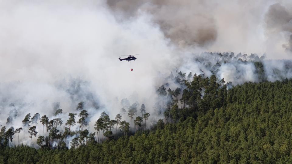 HANDOUT - A helicopter of the German Federal Police is fighting fire at a forest near Dahme-Spreewald, south of Berlin, Monday, June 24, 2019. Germany expects the hottest days of the year so far this week. (Bundespolizei/dpa via AP)