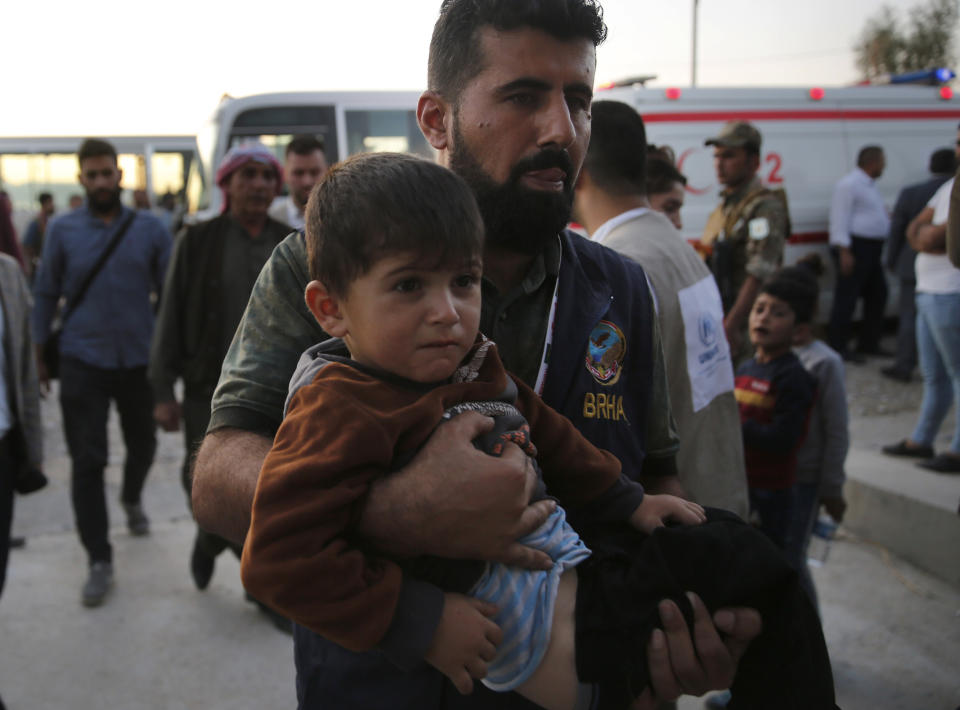 An Iraqi Kurdish humanitarian worker carries a Syrian boy, who is newly displaced with his family by the Turkish military operation in northeastern Syria, at the Bardarash camp, north of Mosul, Iraq, Wednesday, Oct. 16, 2019. The camp used to host Iraqis displaced from Mosul during the fight against the Islamic State group and was closed two years ago. The U.N. says more around 160,000 Syrians have been displaced since the Turkish operation started last week, most of them internally in Syria. (AP Photo/Hussein Malla)