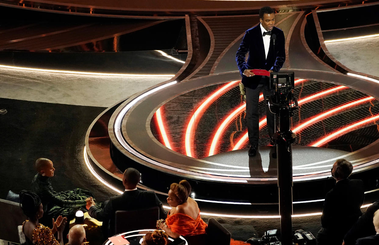 Chris Rock, right, speaks onstage as Jada Pinkett Smith and Will Smith, bottom left, look on after Smith slapped Rock at the Oscars in Los Angeles, on March 27, 2022.