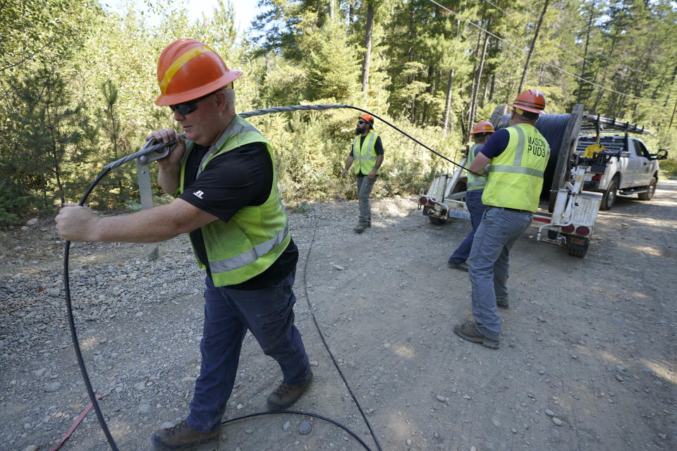 FILE - In this Wednesday, Aug. 4, 2021, file photo, Carl Roath, left, a worker with the Mason County (Wash.) Public Utility District, pulls fiber optic cable off of a spool, as he works with a team to install broadband internet service to homes in a rural area surrounding Lake Christine near Belfair, Wash. (AP Photo/Ted S. Warren, File)