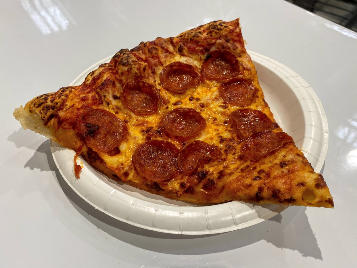 Slice of a pepperoni pizza on a white paper plate at the Costco food court, on a white table