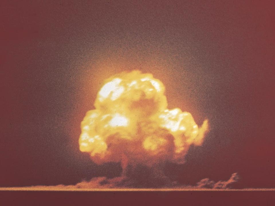 trinity nuclear bomb test distant yellow mushroom cloud erupting into orange sky