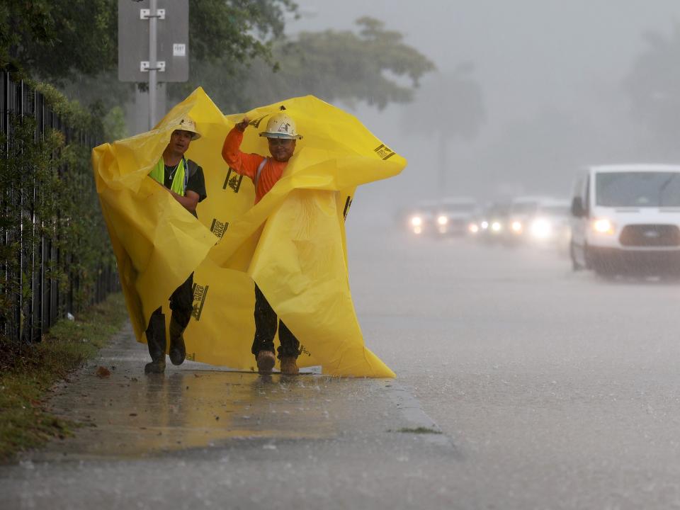 Workers use a tarp to protect themselves from the rain on April 12, 2023 in Dania Beach, Florida.