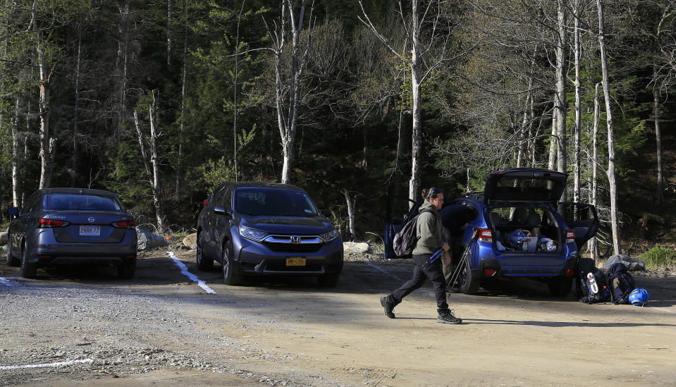 A hiker walks through the parking lot at the Adirondack Mountain Reserve trailhead, Saturday, May 15, 2021, in St. Huberts, N.Y. A free reservation system went online recently to control the growing number of visitors packing the parking lot and tramping on the trails through the private land of the Adirondack Mountain Reserve. The increasingly common requirements, in effect from Maui to Maine, offer a trade-off to visitors, sacrificing spontaneity and ease of access for benefits like guaranteed parking spots and more elbow room in the woods. (AP Photo/Julie Jacobson)