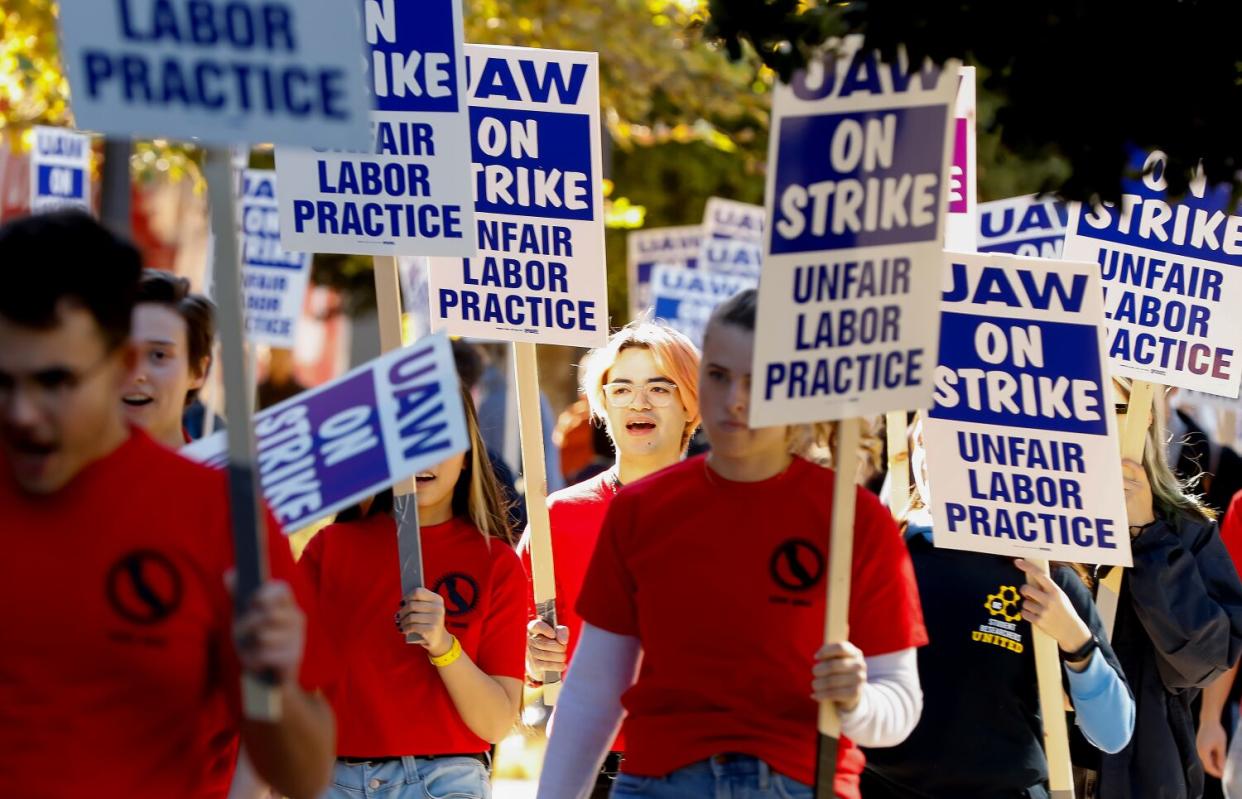 Picketers in red shirts hold signs outdoors.