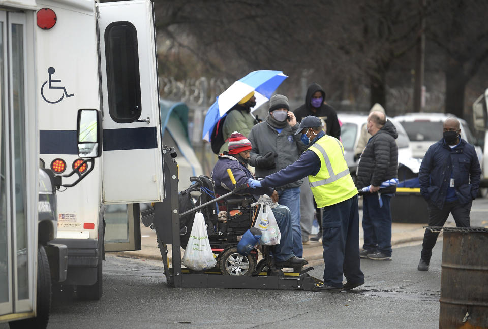 A man is loaded onto a bus for a trip to a hotel on Thursday, Feb. 18, 2021 in Charlotte, N.C. Residents of the homeless encampment "Tent City" are being required to vacate the area within 72 hours after health risks from rodent infestation was found in the area. (Jeff Siner/The Charlotte Observer via AP)