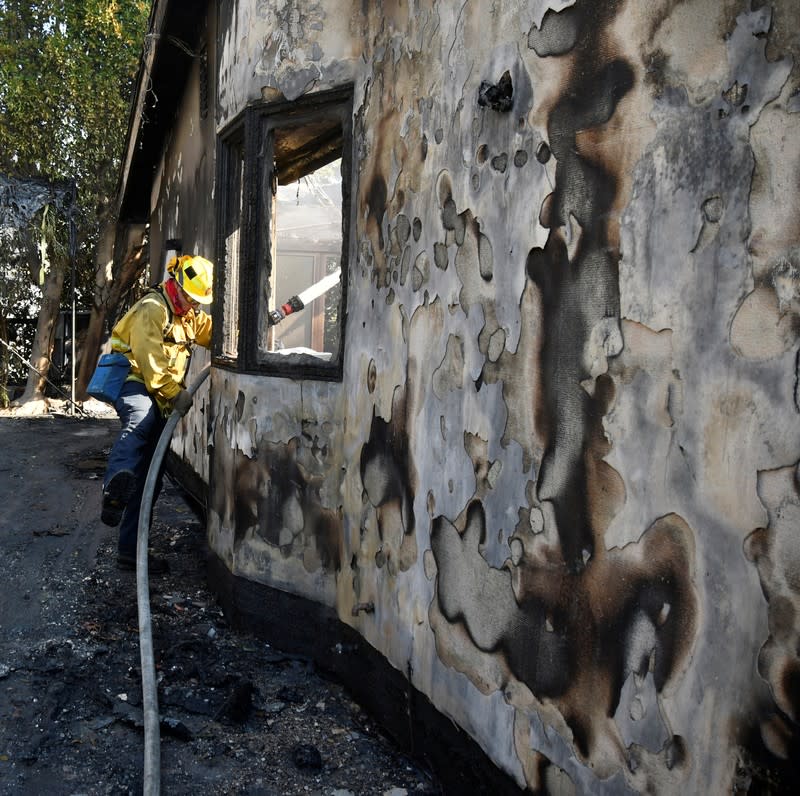 A firefighter douses water on a house after it was burned by the wind-driven Getty Fire in West Los Angeles, California