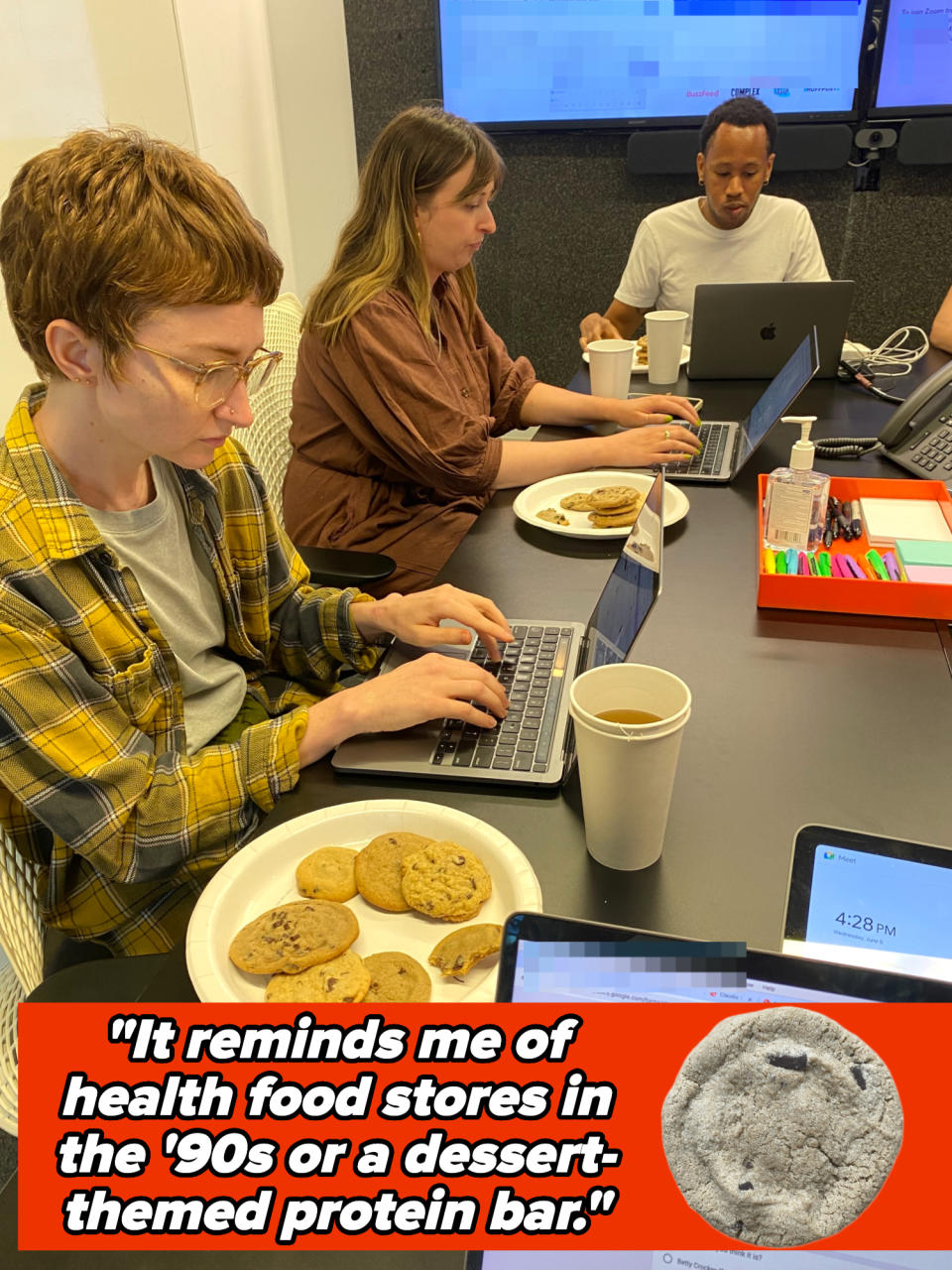 Three people work at a table with laptops and cookies. There's a printed text saying, "It reminds me of health food stores in the '90s or a dessert-themed protein bar."