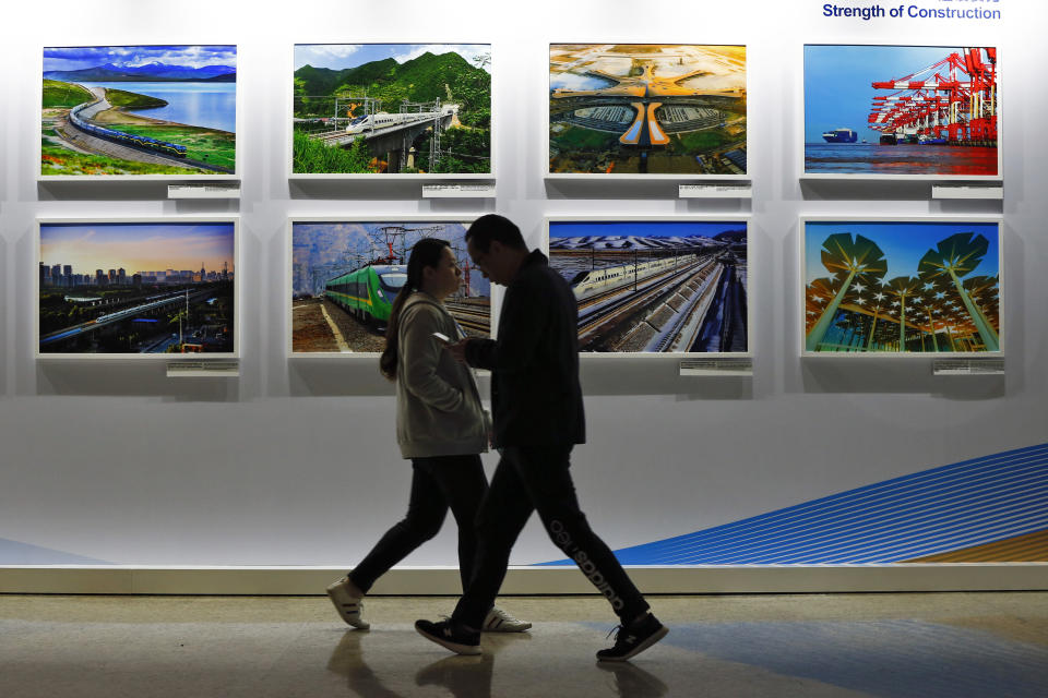 FILE - In this Saturday, April 27, 2019 file photo, people walk by a display board showcasing China's sweeping infrastructure-building projects at the media center of the Belt and Road Forum in Beijing. African leaders in 2020 are asking what China can do for them as the coronavirus pandemic threatens to destroy economies across a continent where Beijing is both the top trading partner and top lender. (AP Photo/Andy Wong, File)