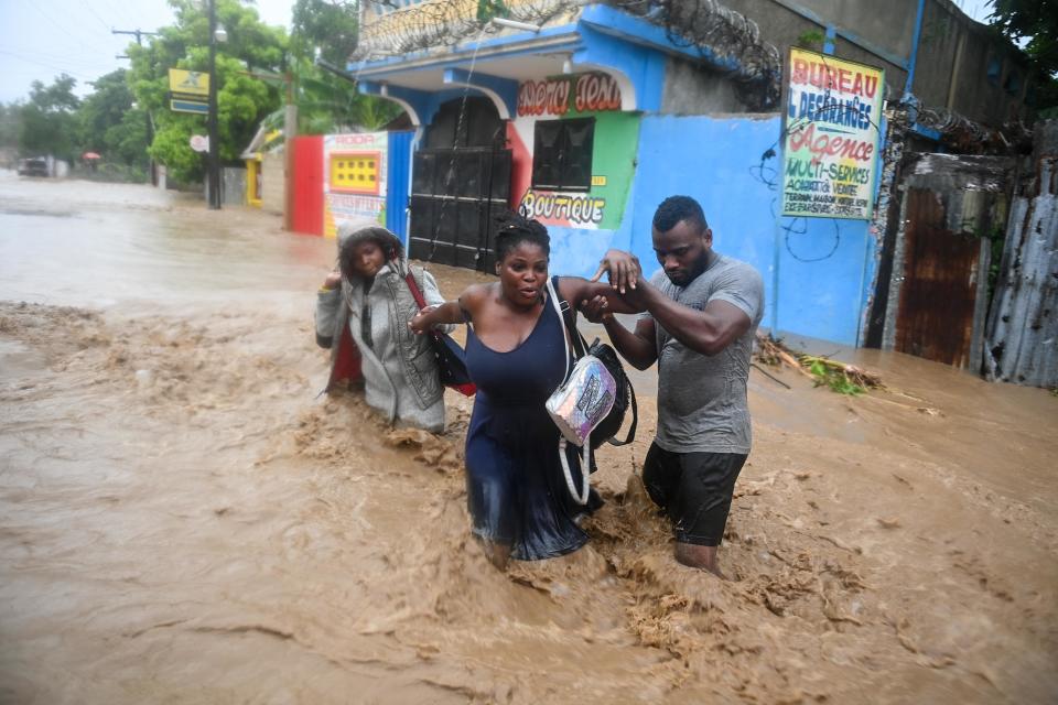 Three people wade through a nearly waist-high flooded road.