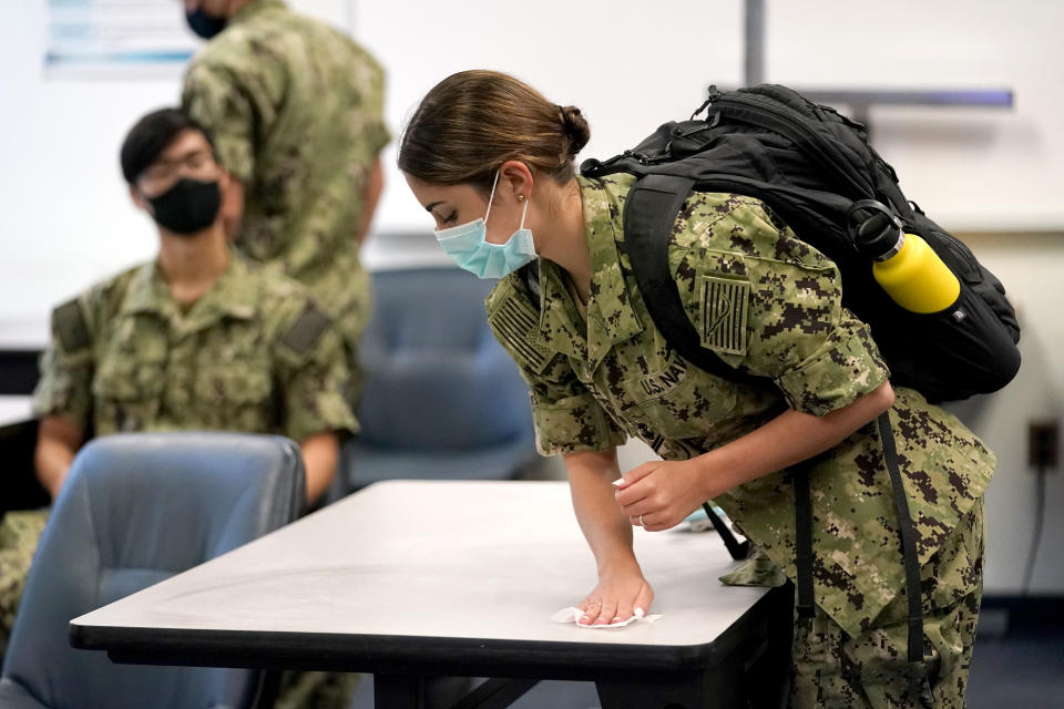 A midshipwoman uses a sanitizing wip to clean her desk before the start of a leadership class at the U.S. Naval Academy, Monday, Aug. 24, 2020, in Annapolis, Md. Under the siege of the coronavirus pandemic, classes have begun at the Naval Academy, the Air Force Academy and the U.S. Military Academy at West Point. But unlike at many colleges around the country, most students are on campus and many will attend classes in person. (AP Photo/Julio Cortez)