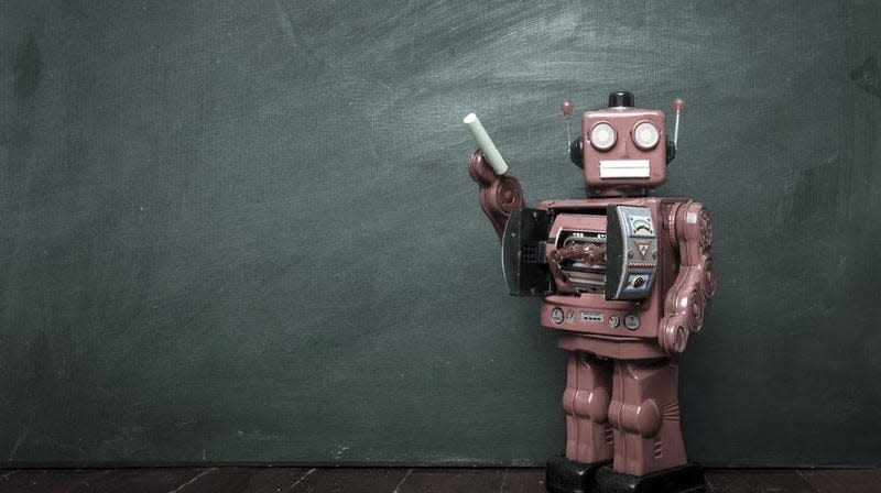 A robot holds a piece of chalk to a blackboard.