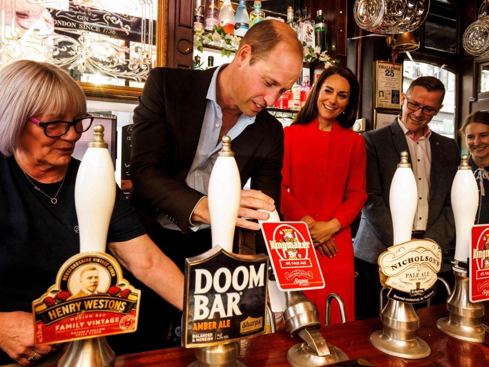 Prince William, Prince of Wales (2nd L) flanked by Britain's Catherine, Princess of Wales (C), serves a beer during a visit of the Dog & Duck Pub in Soho, central London, on May 4, 2023