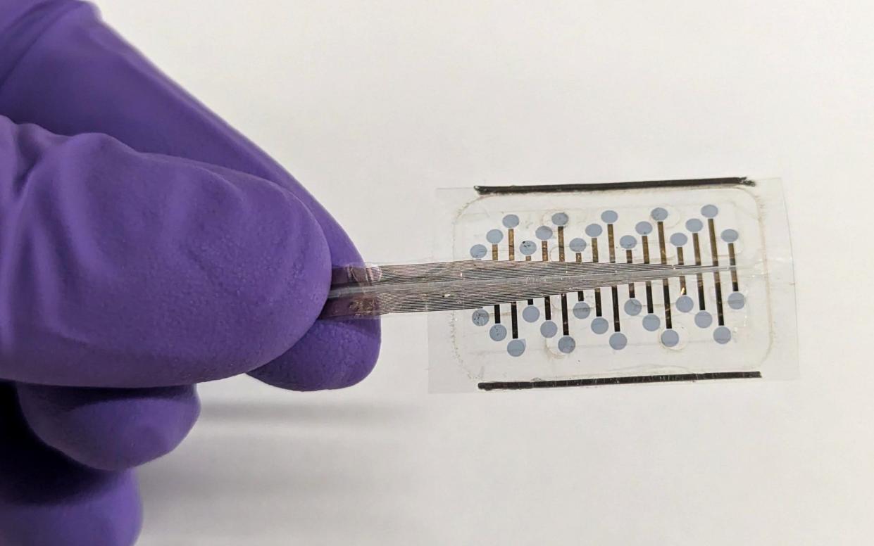 A hand in a surgical glove holds the small, transparent implant in tweezers