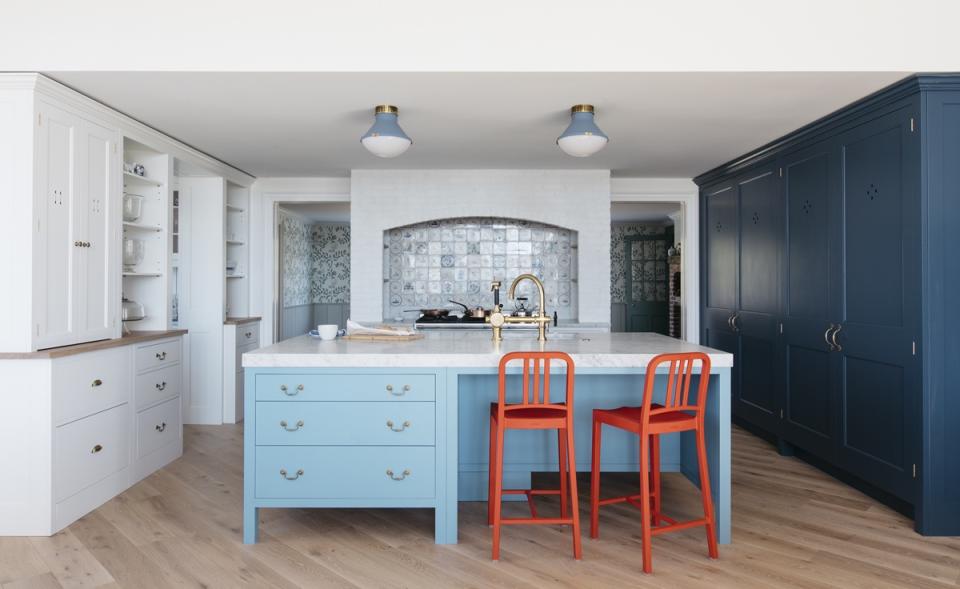 Kitchen island ideas painted pale blue with bright orange chairs, in a white kitchen with one dark blue painted row of storage.