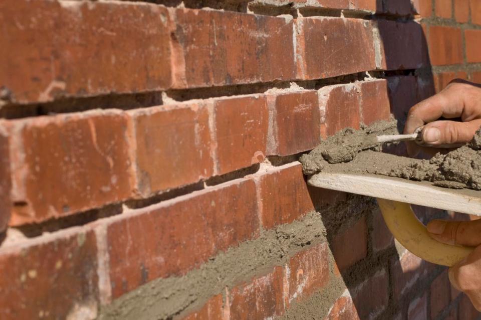 A close up of a worker's hand repairing a brick wall.