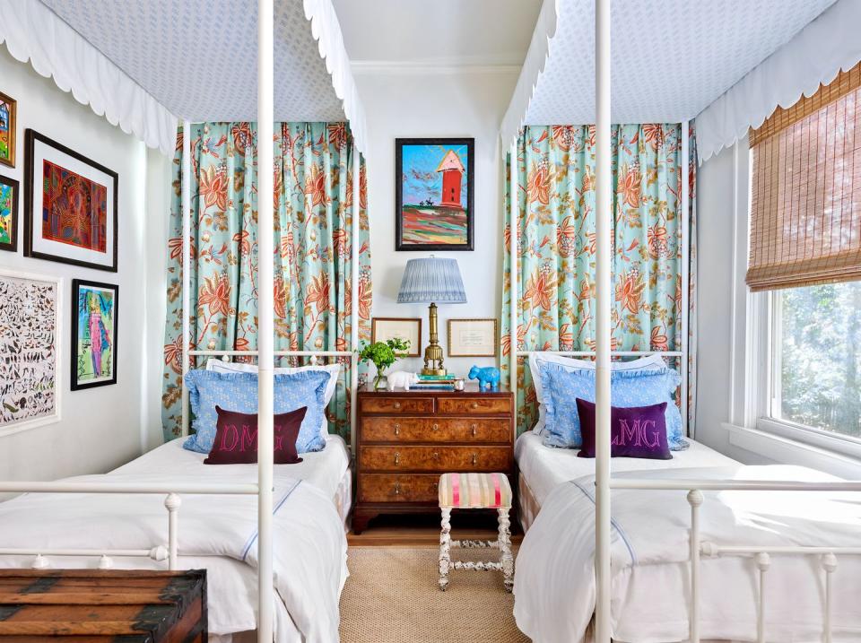 bedroom with twin canopied beds next to each other with art on the walls and a large window to the right