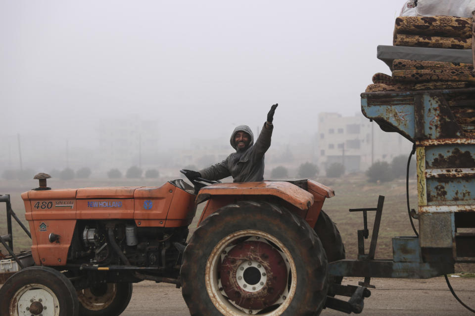 A man waves to a photographer as civilians ride in a truck as they flee Maaret al-Numan, Syria, ahead of a government offensive, Monday, Dec. 23, 2019. (AP Photo/Ghaith al-Sayed)
