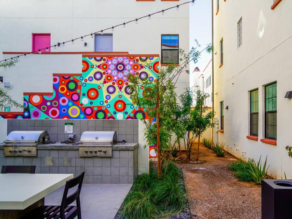 Culdesac Tempe: A courtyard with white buildings and a table and grills on the left in front of a colorful mural