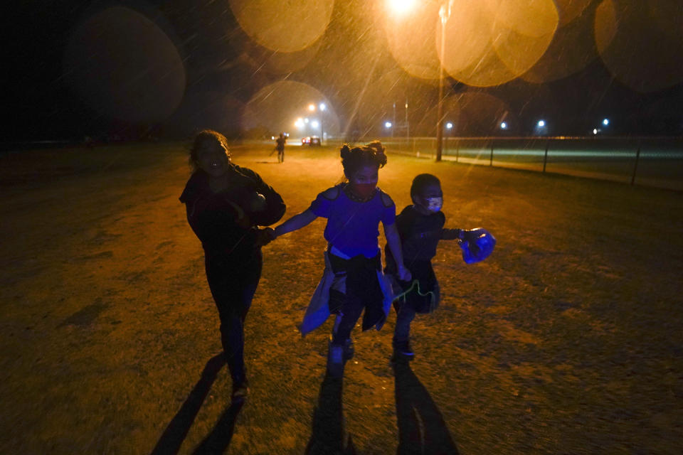 FILE - Three young migrants hold hands as they run in the rain at an intake area after turning themselves in upon crossing the U.S.-Mexico border in Roma, Texas, May 11, 2021. Biden took office on Jan. 20 and almost immediately, numbers of migrants exceeded expectations. (AP Photo/Gregory Bull, File)